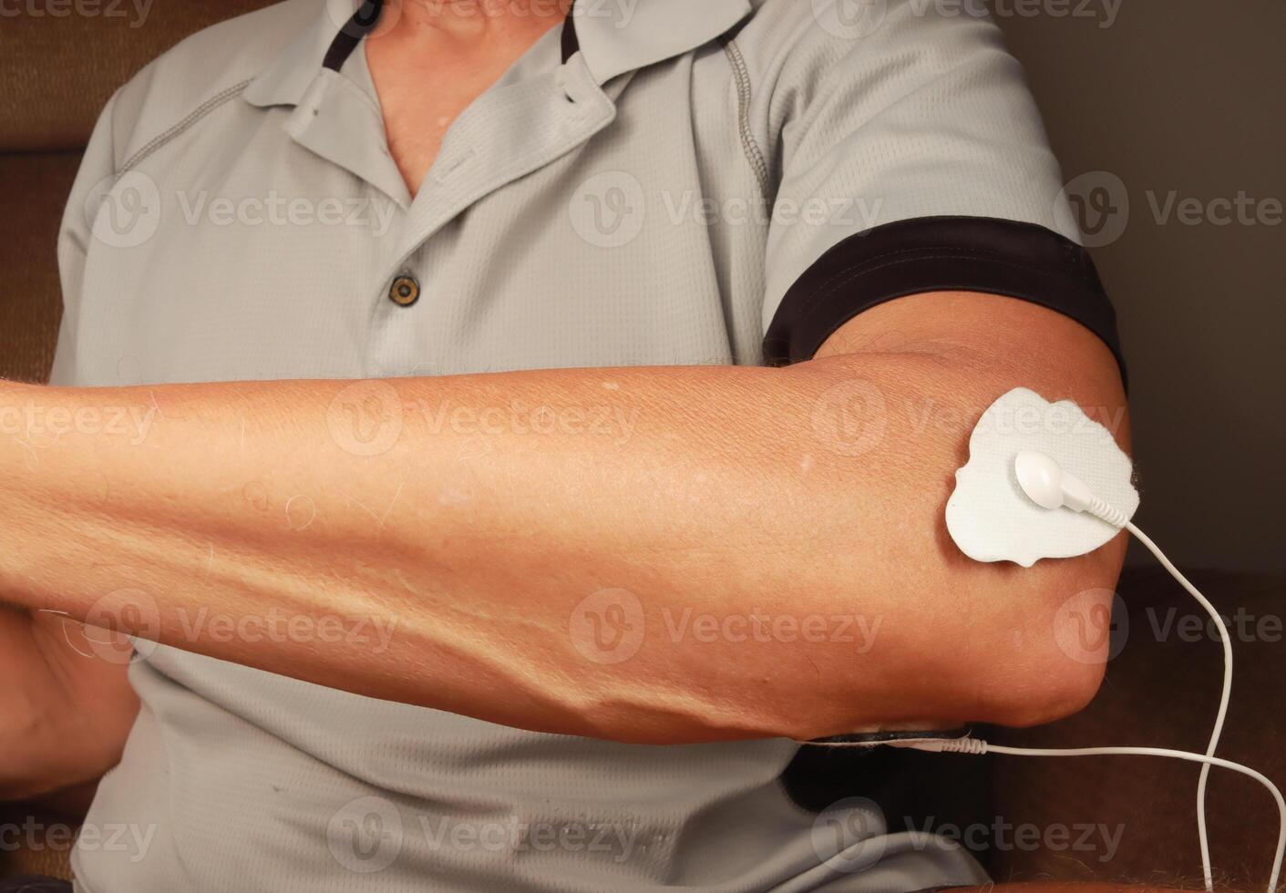 Man using an Electro Therapy Massager or Tens Unit on his elbow for pain relief of Muscles and Joint photo