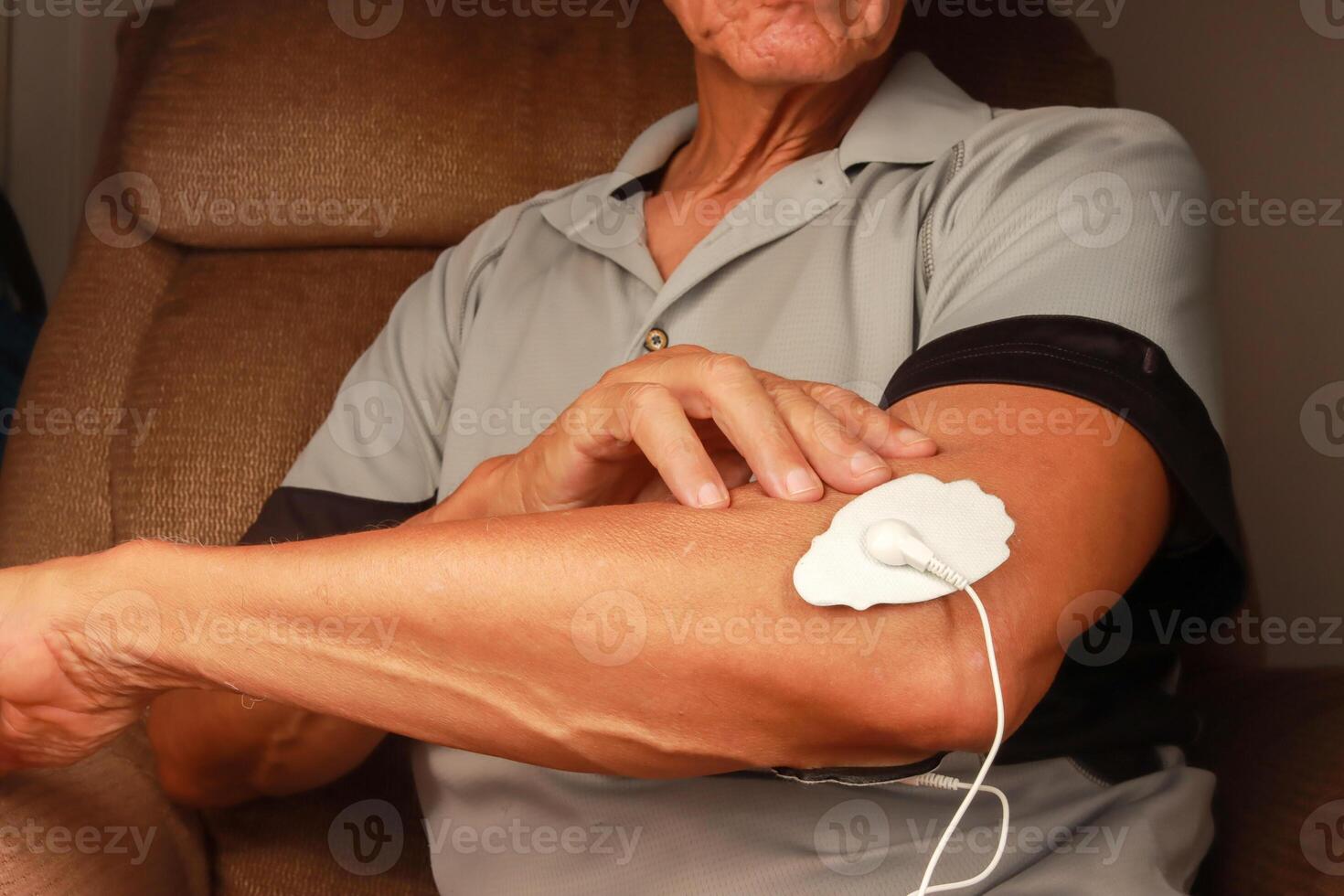 hombre utilizando un electro terapia masajeador o decenas unidad en su codo para dolor alivio de músculos y articulación foto