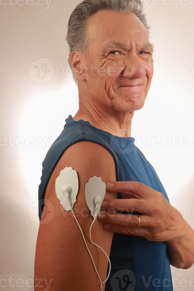 hombre utilizando un electro terapia masajeador o decenas unidad en su deltoides para dolor alivio para músculos y articulaciones foto