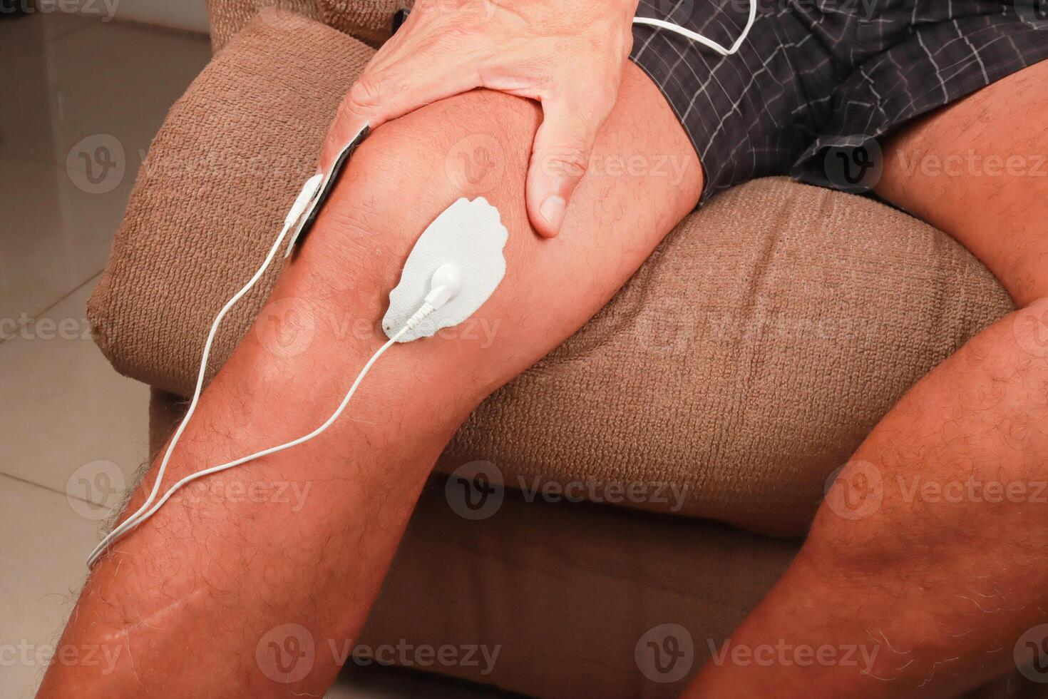hombre utilizando un electro terapia masajeador o decenas unidad en su rodilla para dolor alivio de músculos y articulación foto