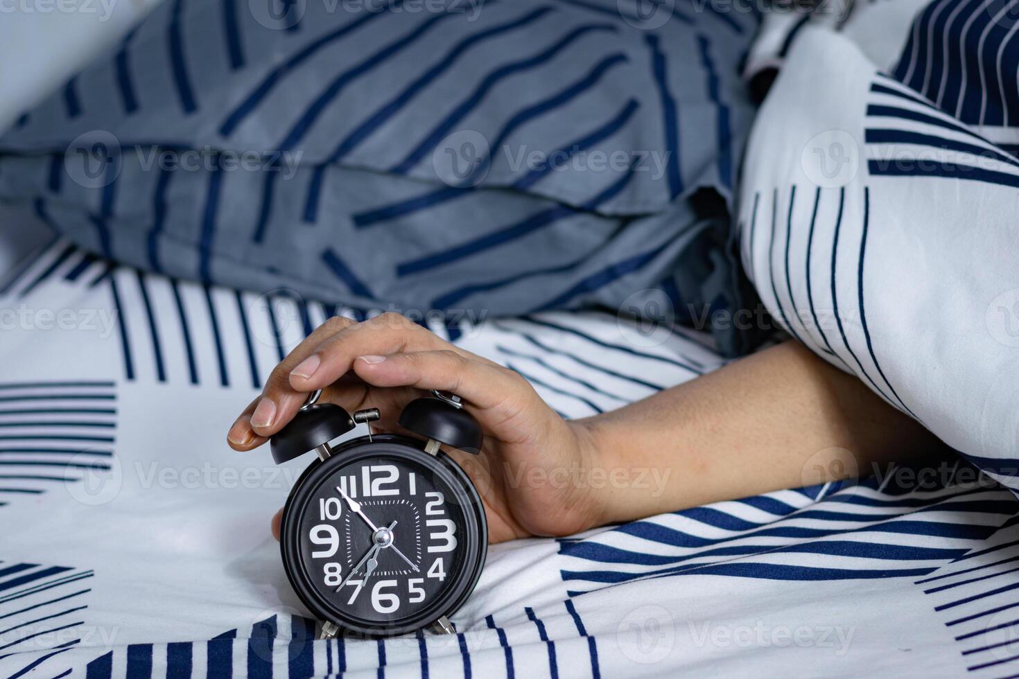 Deadline and Time management concept. Man hands holding Black alarm clock on bed. time to wake up for the morning routine photo
