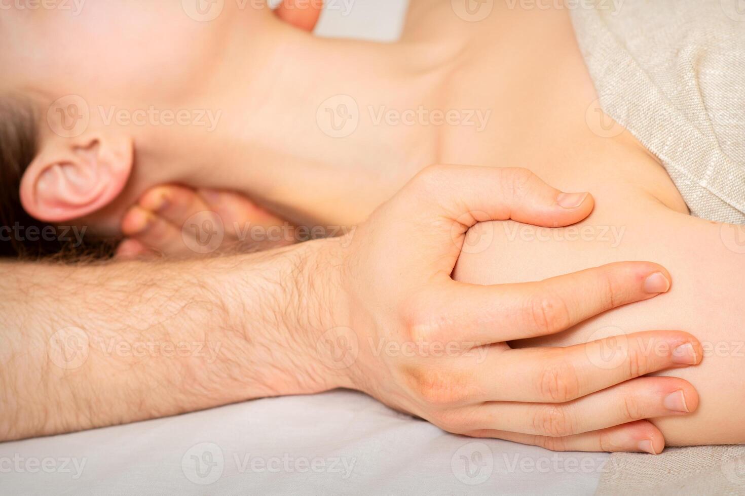 Male masseur massaging shoulder of a young woman lying on a massage table in a spa clinic. photo