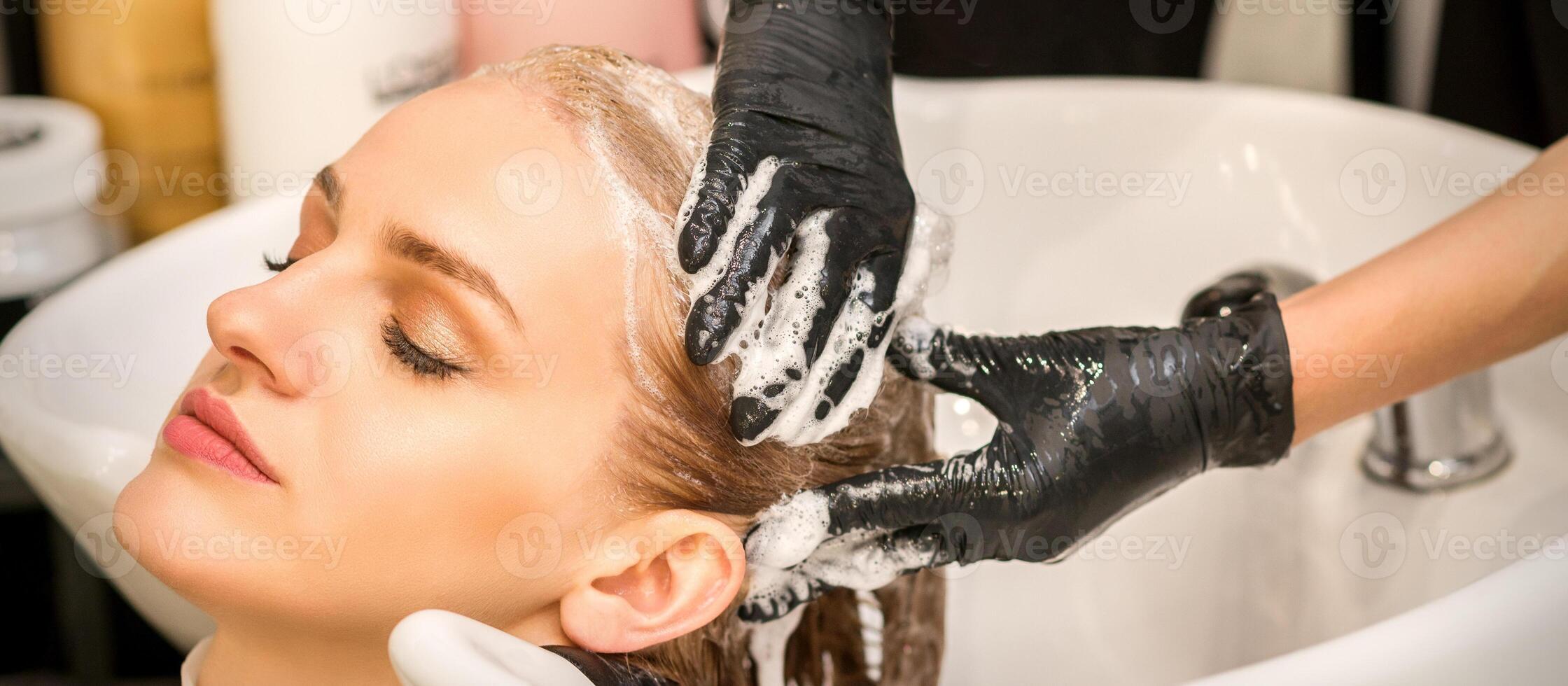 Young caucasian blonde woman having hair washed in the sink at a beauty salon. photo