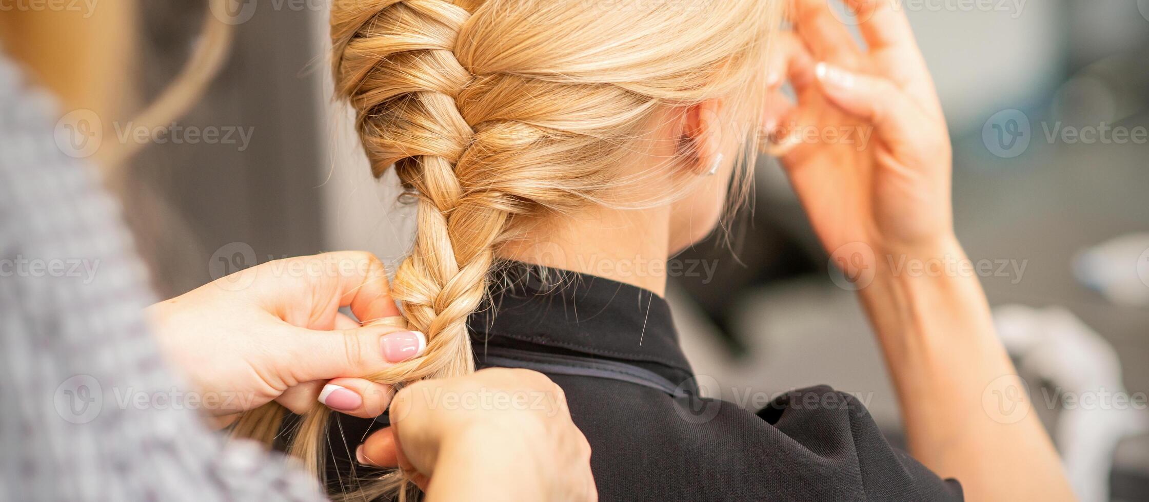 Braiding braid. Hands of female hairdresser braids long braid for a blonde woman in a hair salon. photo