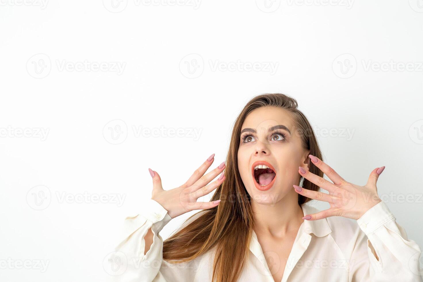 Shocked young caucasian woman with open mouth looking up and expresses surprise isolated over white background. Beautiful surprised brunette woman in studio. photo