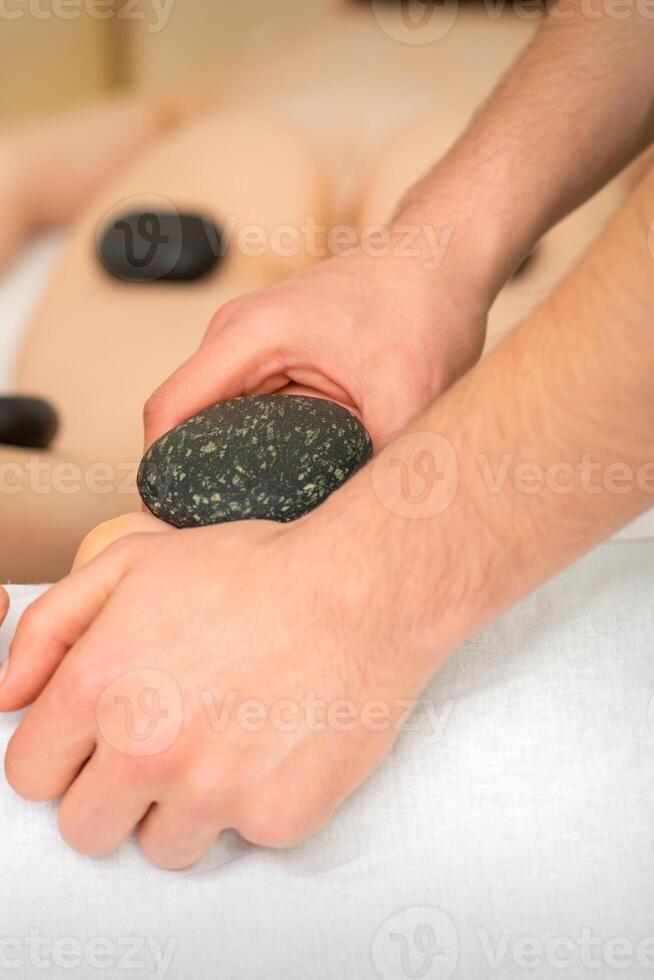 Two masseurs make a foot massage with a hot stone in four hands at the spa. photo