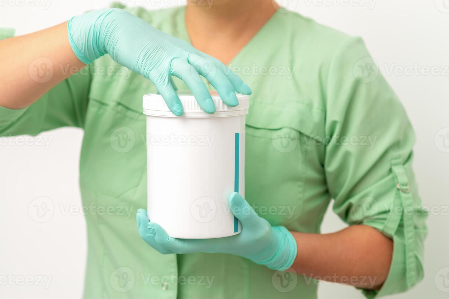 Hands in protective gloves of beautician open a white body cream jar on white background. photo