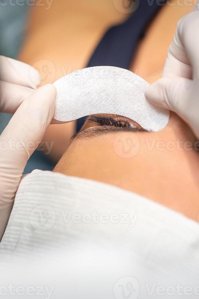 The beautician is gluing a patch under her eyes, before the procedure of eyelash extension. Artificial extended eyelashes. photo