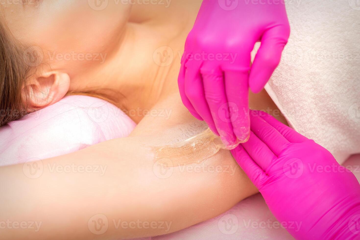 A beautician applies a sugar paste depilation under the female armpit in a beauty salon, close up. photo