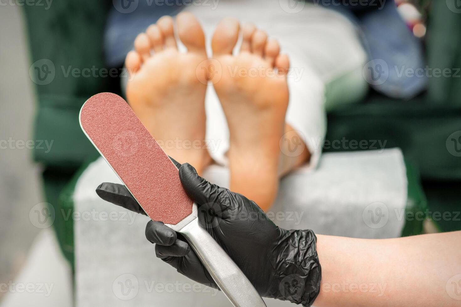 Special grater for scrubbing heels in hands of nail pedicure technician on feet background in beauty salon closeup. photo
