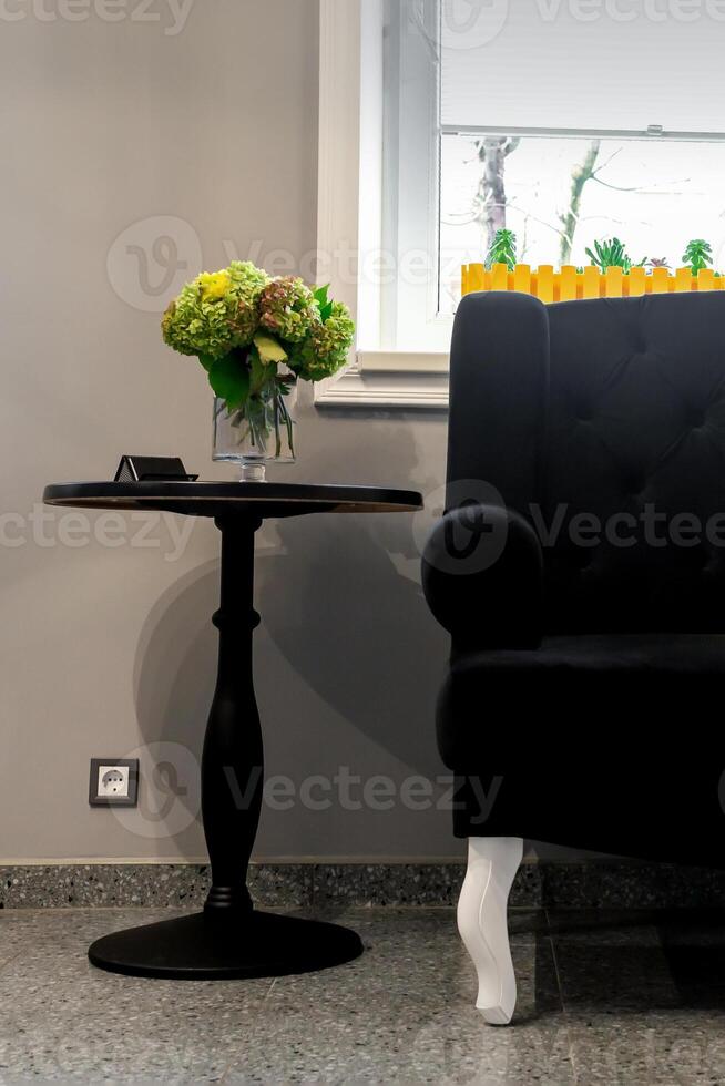 Interior of the beauty room. Black sofa with small yellow pillows and coffee table on a gray wall background with a window. photo