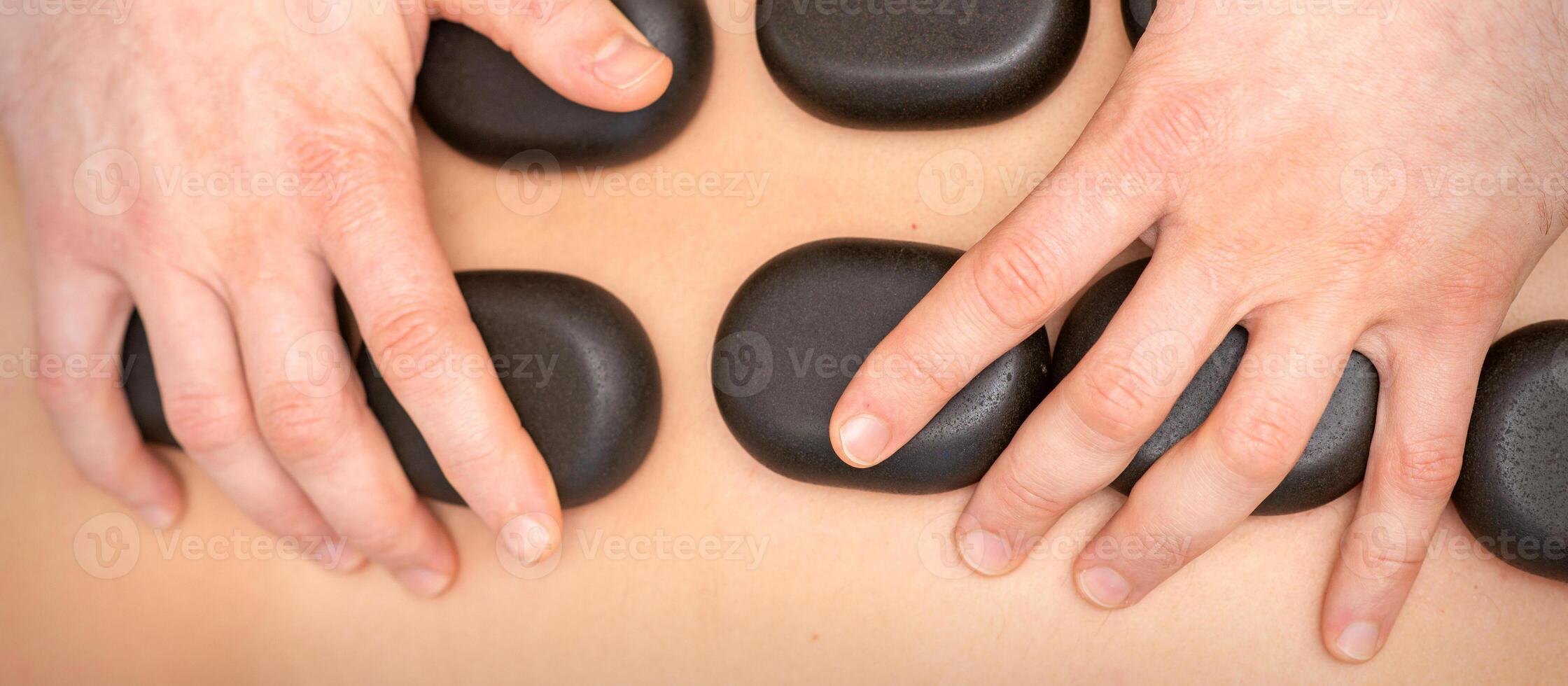 Hot stone massage therapy. Caucasian young man getting a hot stone massage on back at spa salon. photo