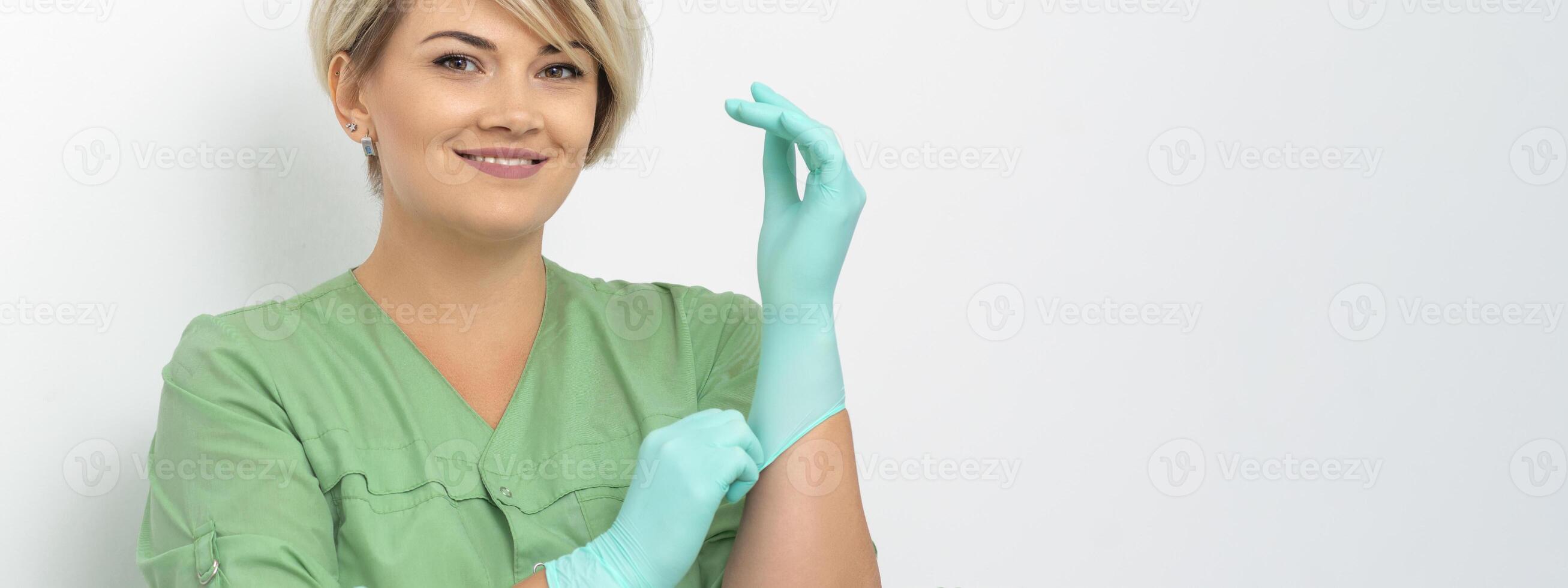 Doctor beautician puts on sterile blue gloves smiling prepares to receive clients on white. photo