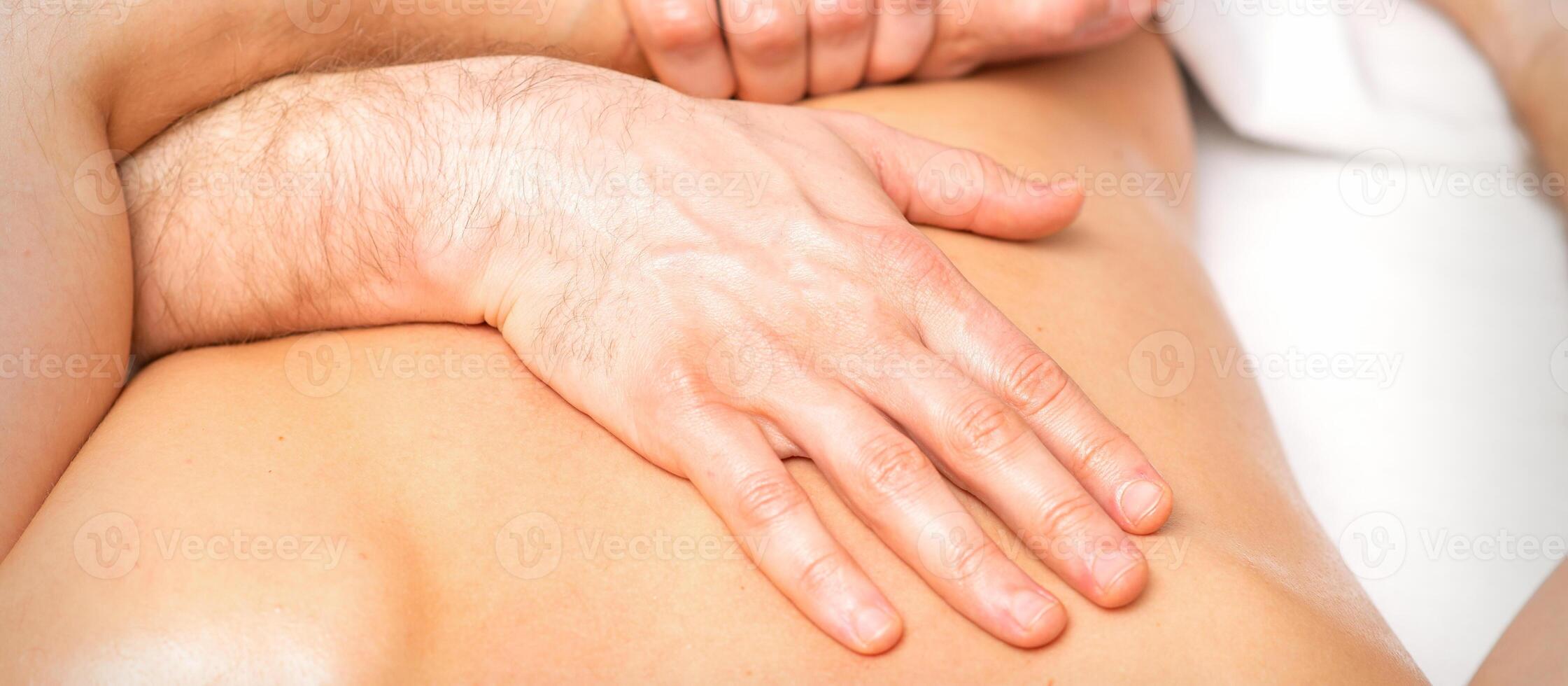 A male physiotherapist stretches the arms on the back of a man lying down, close up. photo