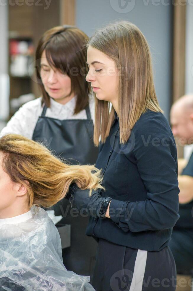 Two female hairstylists prepare long hair of a young woman making curls hairstyle in a beauty salon. photo