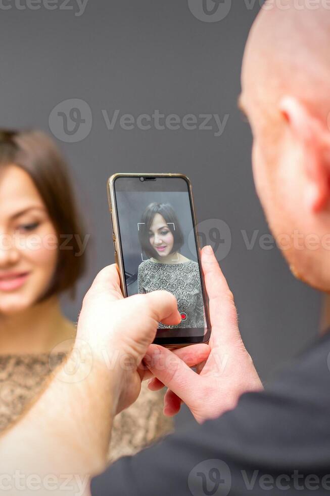 The hairdresser takes pictures of a woman finished short hairstyle on dark background. photo