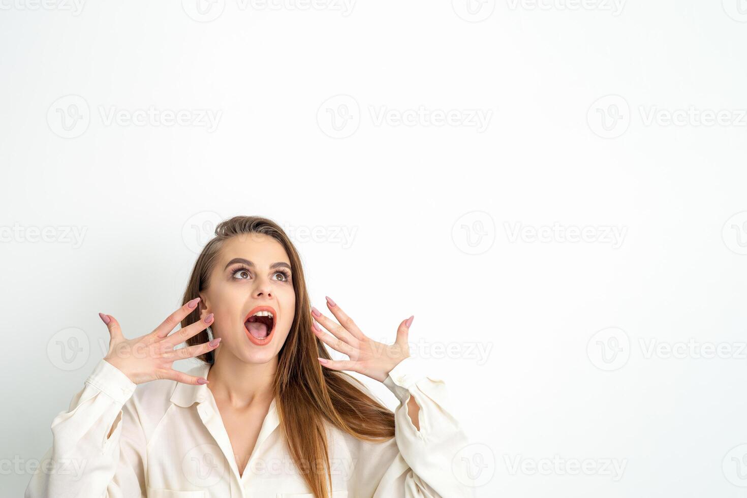 Shocked young caucasian woman with open mouth looking up and expresses surprise isolated over white background. Beautiful surprised brunette woman in studio. photo