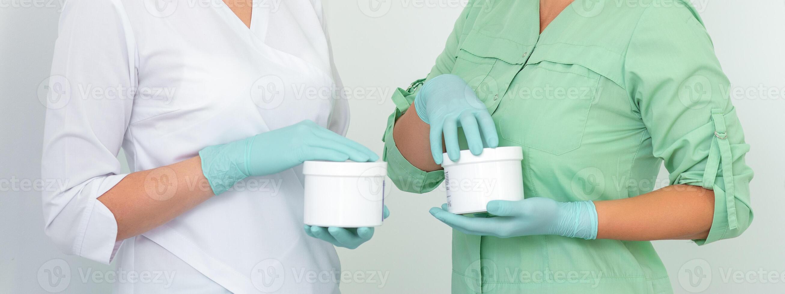 Two cosmeticians with jars of wax for depilation smiling against a white background. Natural product for hair removal. Copy space. photo