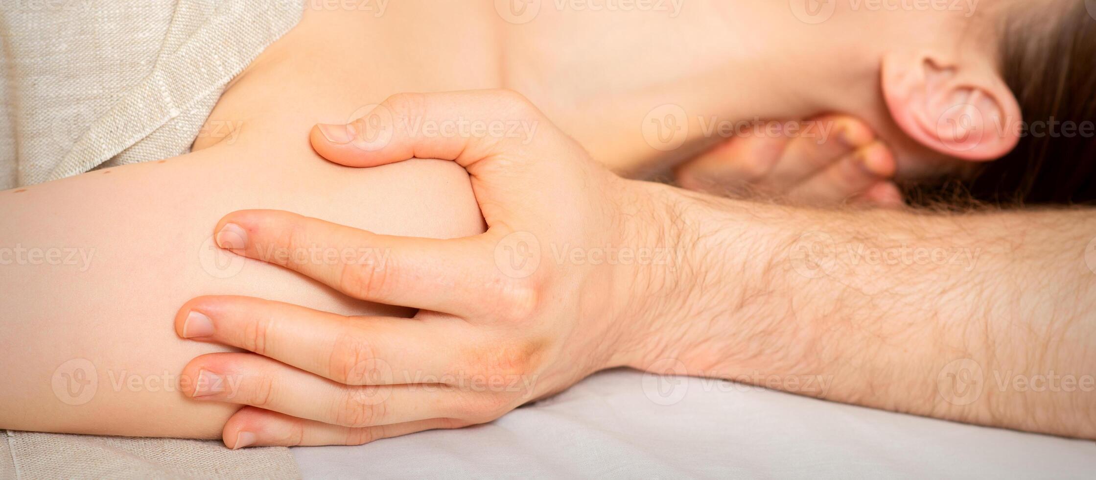 Male masseur massaging shoulder of a young woman lying on a massage table in a spa clinic. photo