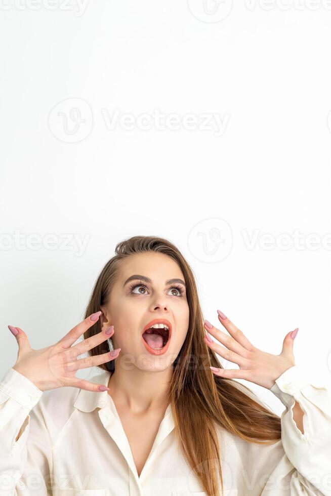 Shocked young caucasian woman with open mouth looking up and expresses surprise isolated over white background. Beautiful surprised brunette woman in studio. photo