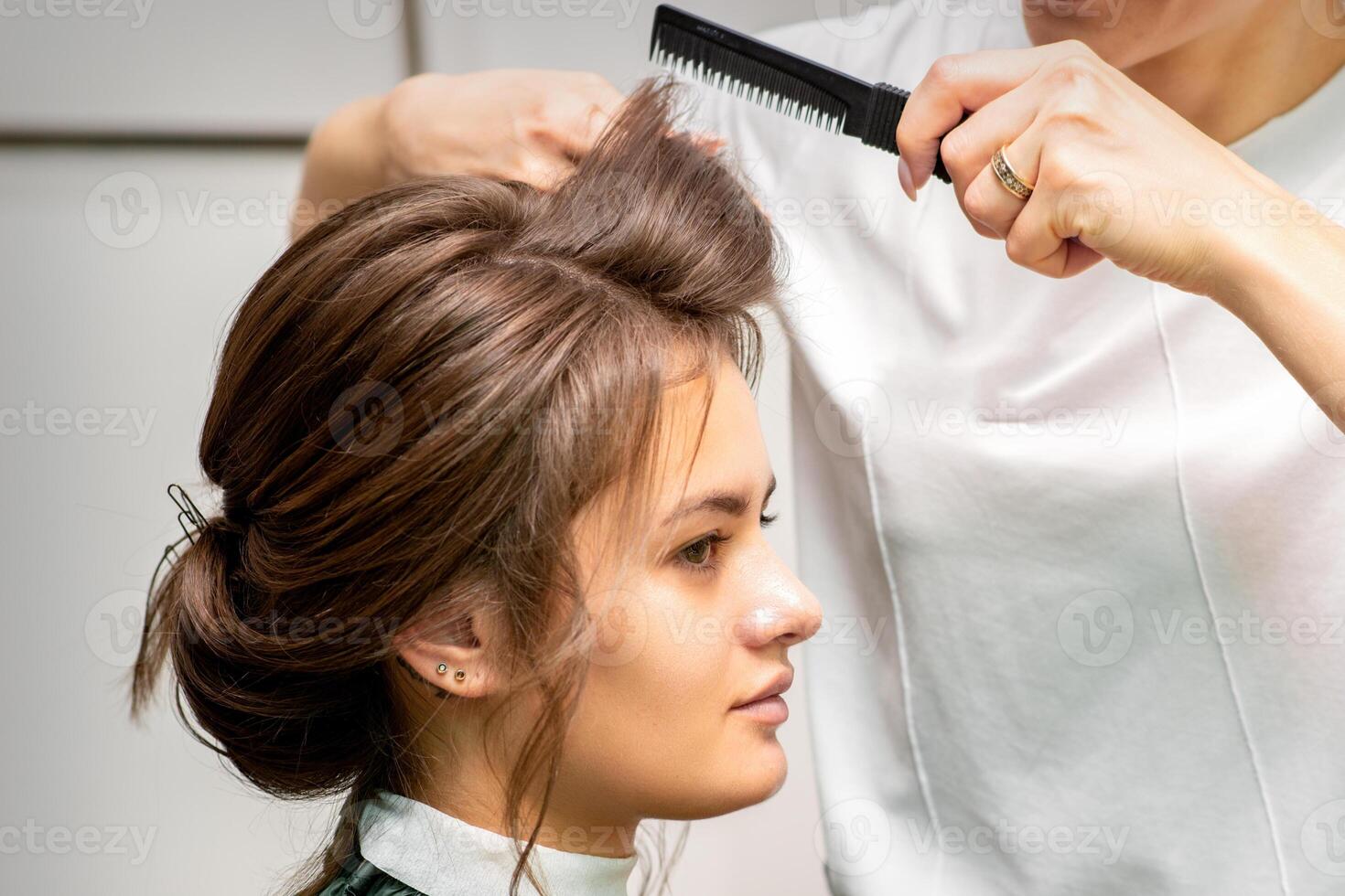 Professional hairdresser doing hairstyle for a beautiful brunette young woman with long hair. Concept of fashion and beauty. photo