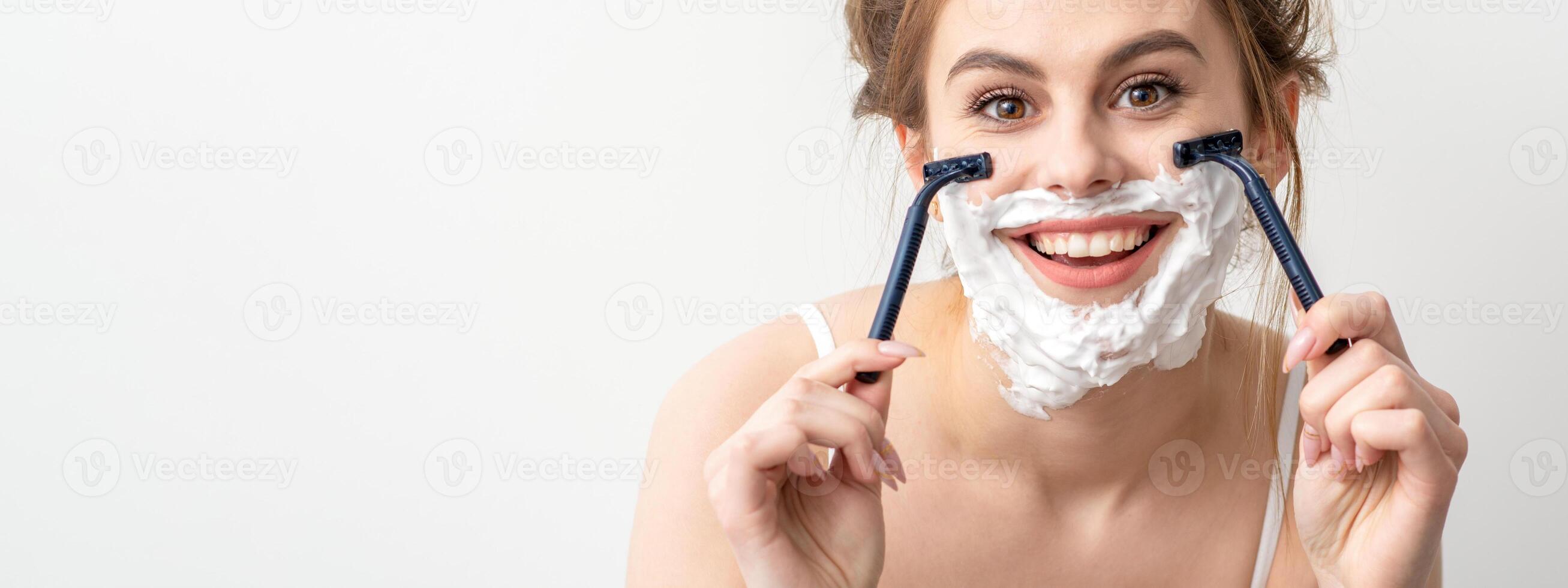 hermosa joven caucásico mujer afeitado su cara por maquinilla de afeitar en blanco antecedentes. bonito sonriente mujer con afeitado espuma y maquinilla de afeitar en su rostro. foto