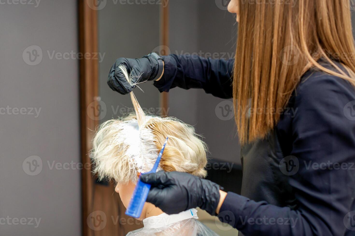 Coloring female hair in the hair salon. Young woman having her hair dyed by beautician at the beauty parlor. photo