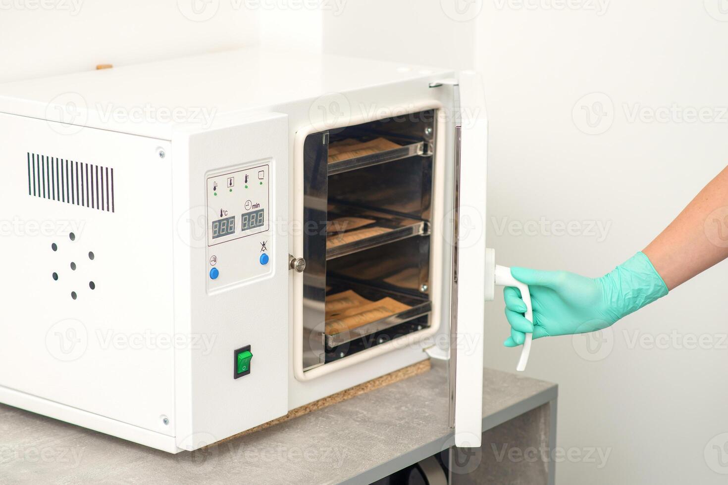 Beautician in protective gloves close the door of the machine for disinfection of tools before the depilation procedure. photo