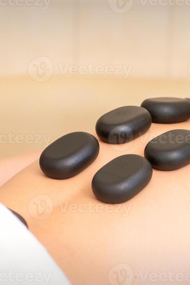 Hot stone massage therapy. Caucasian young man getting a hot stone massage on back at spa salon. photo