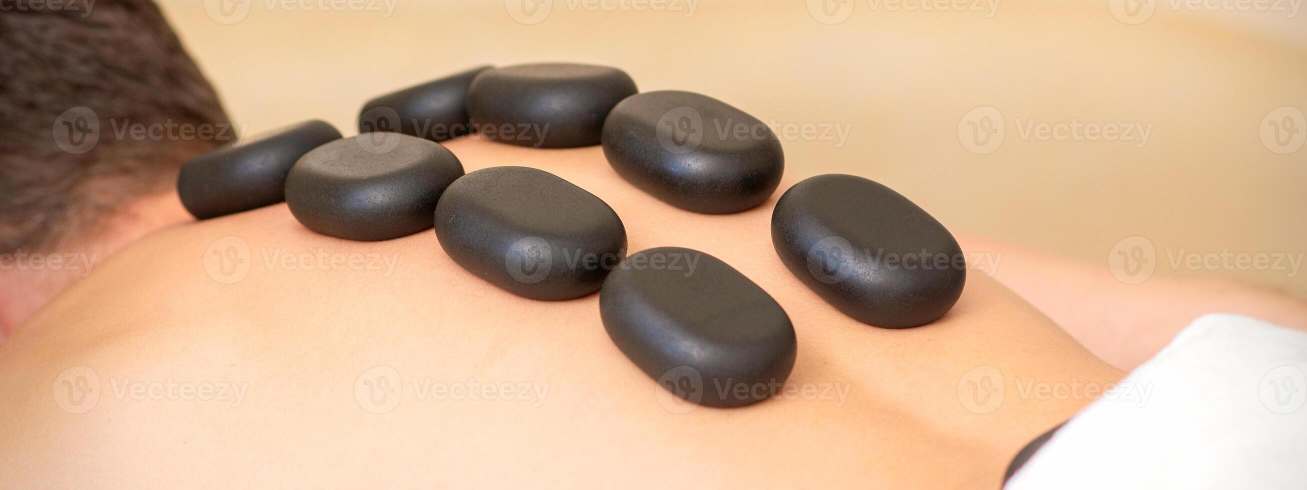 Hot stone massage therapy. Caucasian young man getting a hot stone massage on back at spa salon. photo