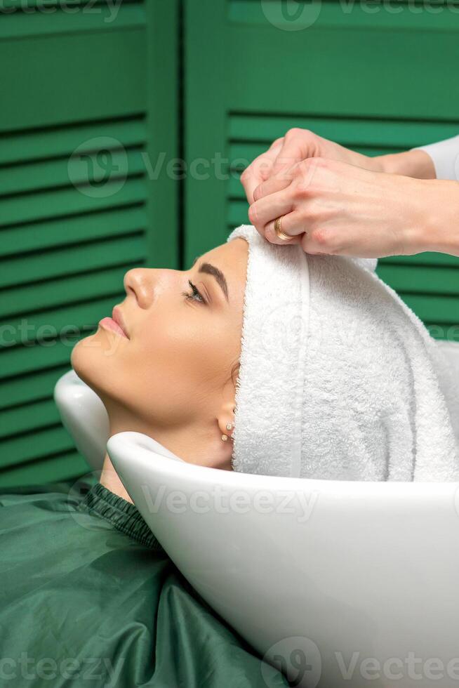 A hairdresser is wrapping a female head in a towel after washing hair in the beauty salon. photo