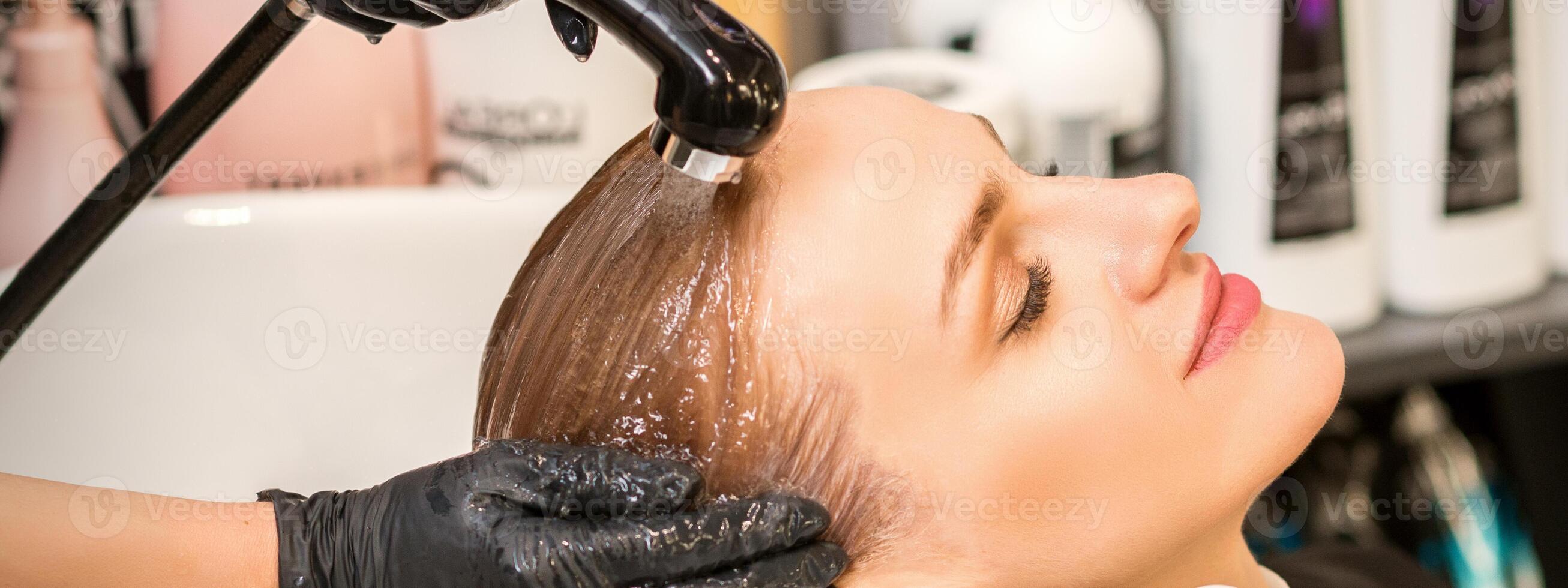 Young caucasian blonde woman having hair washed in the sink at a beauty salon. photo