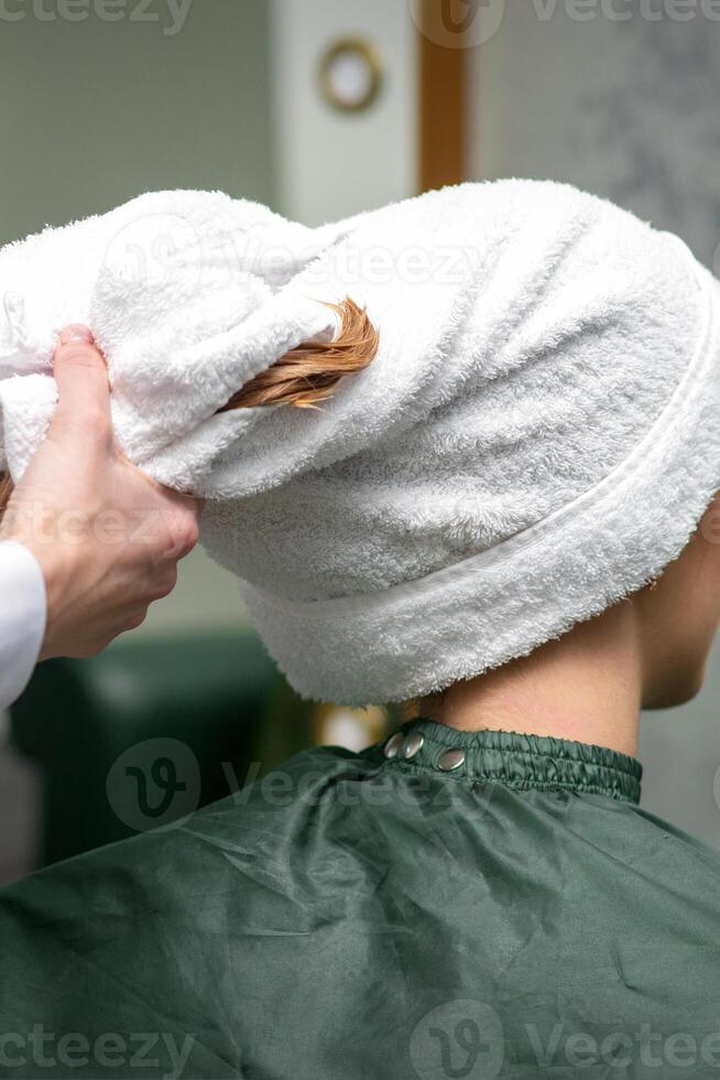 A hairdresser is wrapping the wet hair of the young woman in a towel after washing at the beauty salon. photo