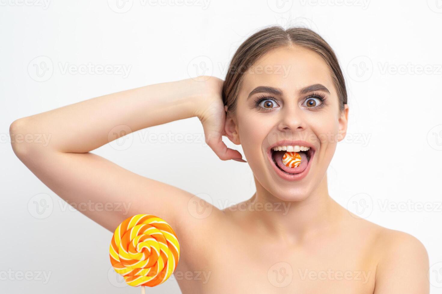 Happy expression young nude woman with candy in mouth holds lollipop near armpit on white background, epilation, depilation, hair removal concept. photo