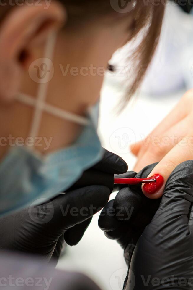 Painting nails of a woman. Hands of Manicurist in black gloves applying red nail polish on female Nails in a beauty salon. photo