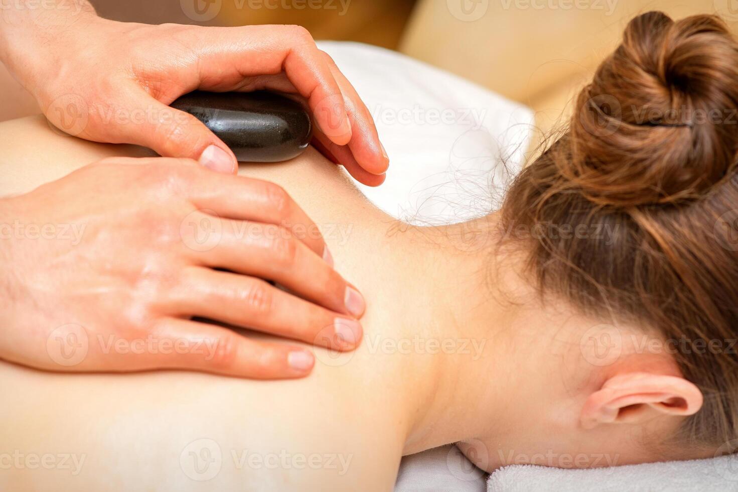 caliente Roca masaje terapia. caucásico joven mujer consiguiendo un caliente Roca masaje en espalda a spa salón. foto