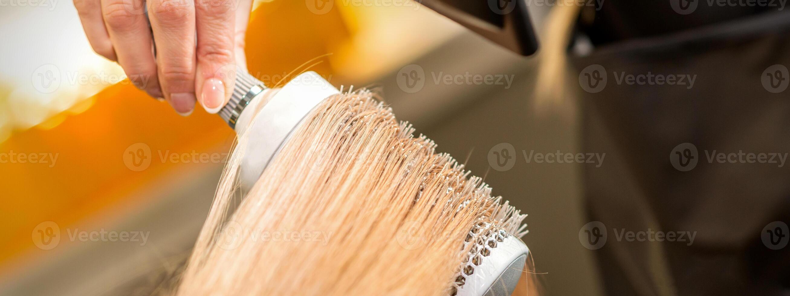 peluquero mano el secado rubio pelo con un secador de pelo y redondo cepillo en un belleza salón. foto