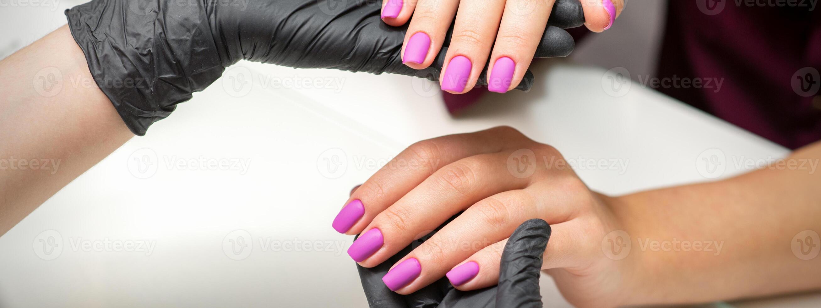 Examination of manicured fingernails. Hands of manicure master in black gloves examining female pink nails in manicure salon. photo