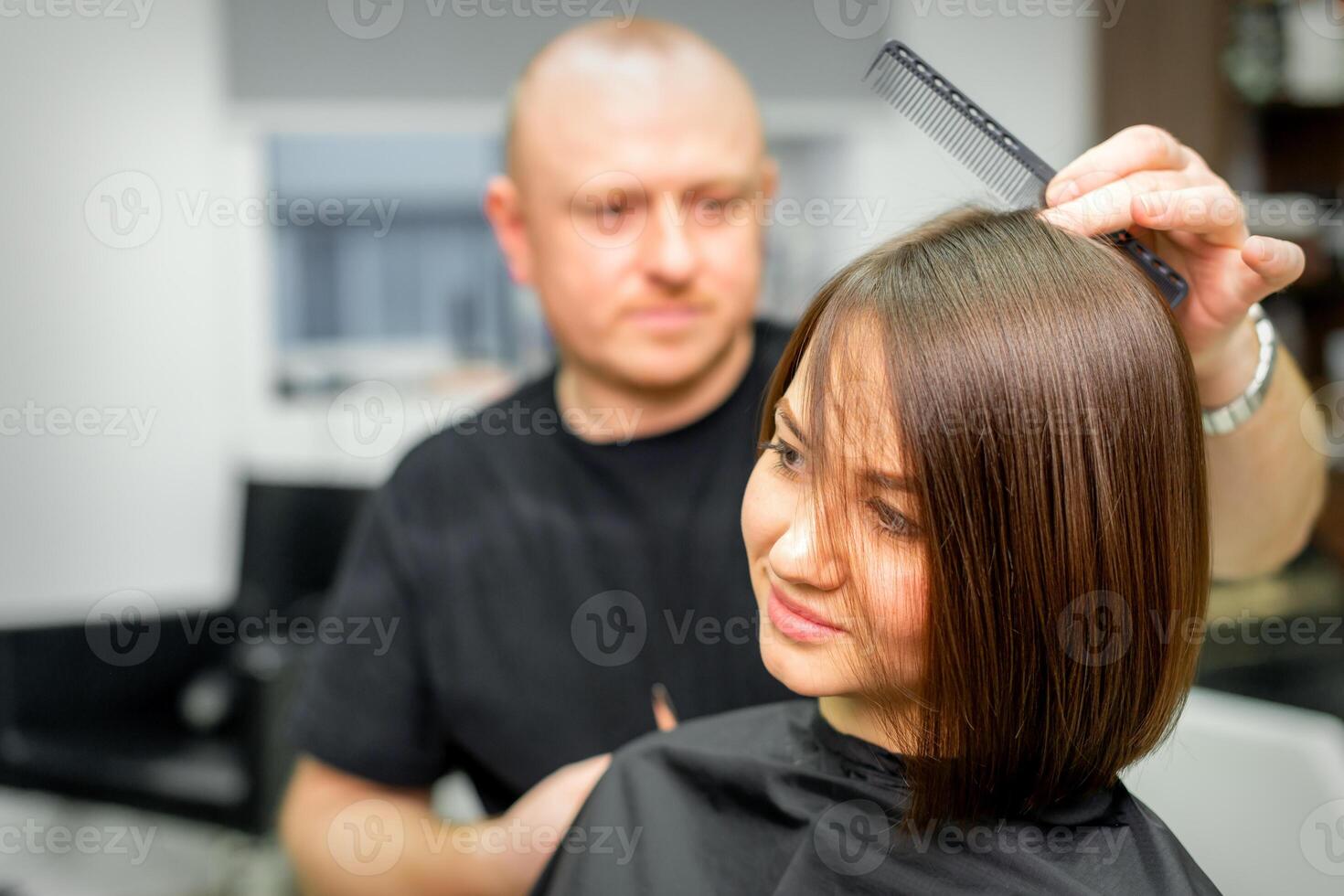 joven caucásico morena mujer teniendo su cortes de cabello por un masculino peluquero a un salón. foto