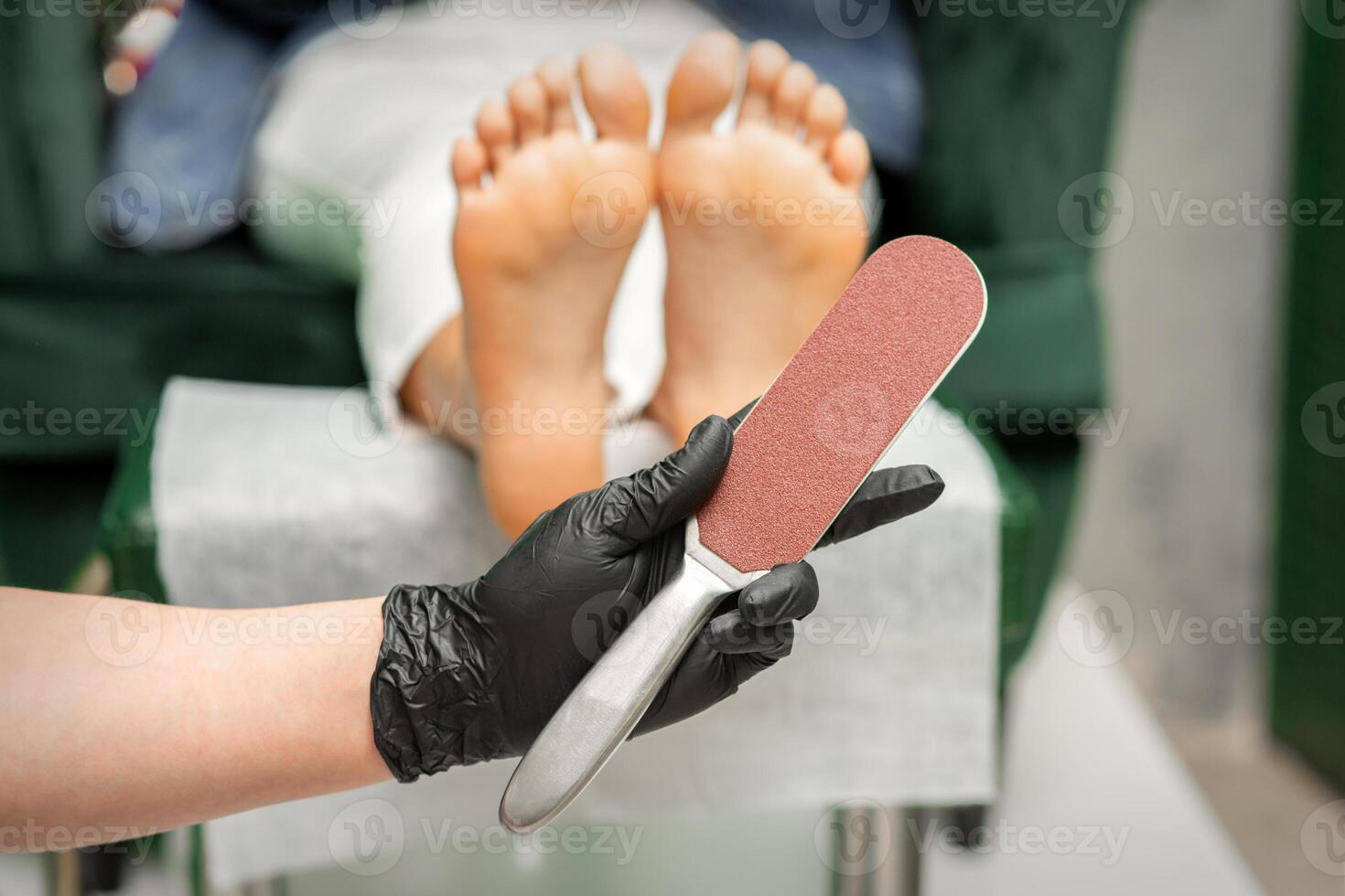 Special grater for scrubbing heels in hands of nail pedicure technician on feet background in beauty salon closeup. photo