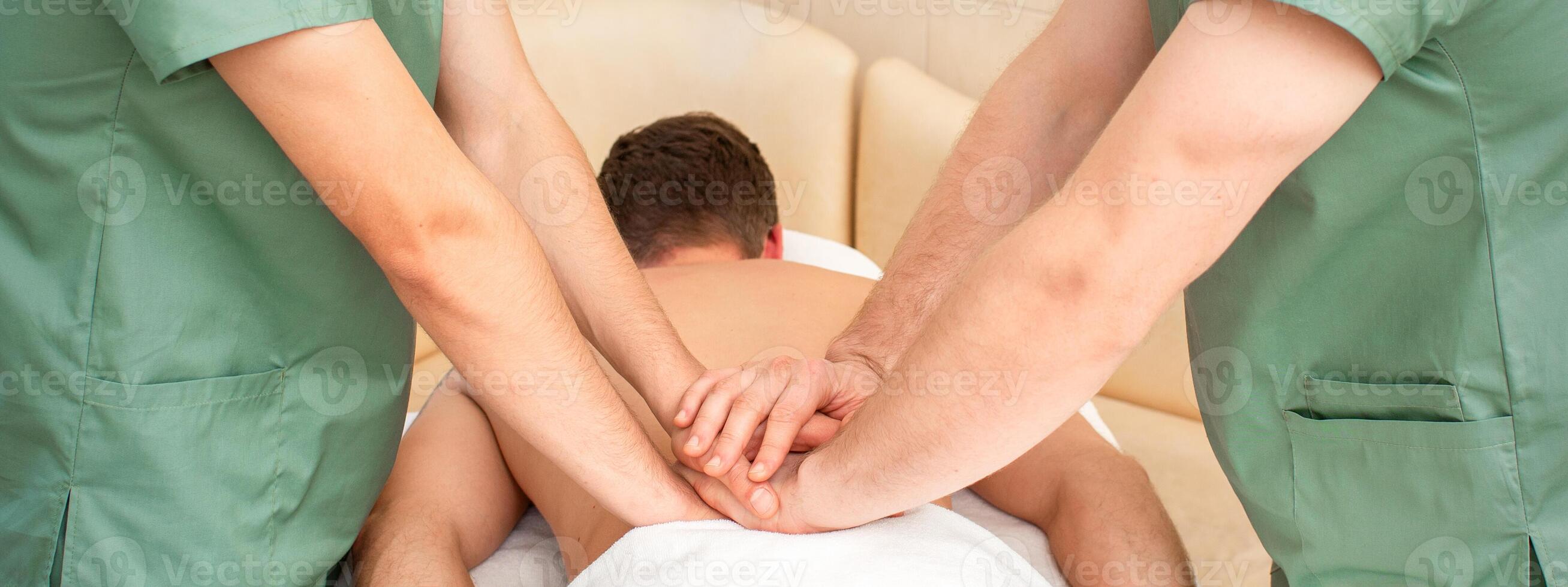 Young man receiving back massage in four hands in spa beauty salon. photo