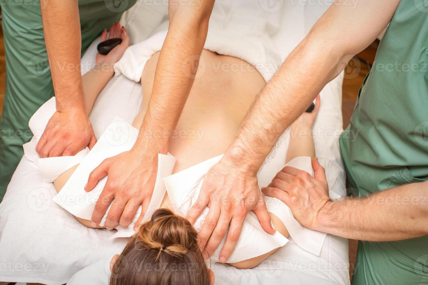 Back Massage with four hands in the spa salon. Two massage therapists make a back massage for a young woman. photo