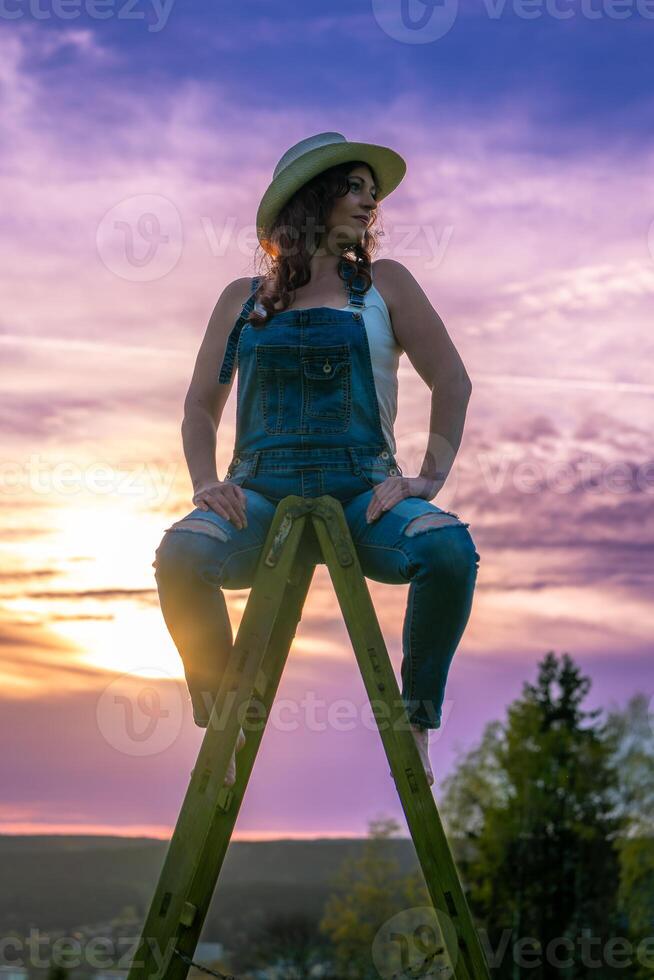 woman in dungarees sitting on a wooden ladder in the sunset photo