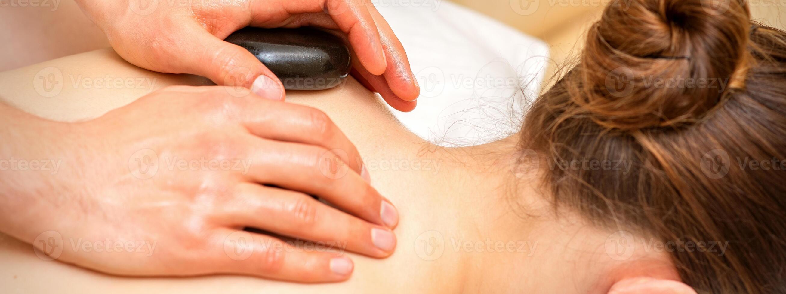 Hot stone massage therapy. Caucasian young woman getting a hot stone massage on back at spa salon. photo