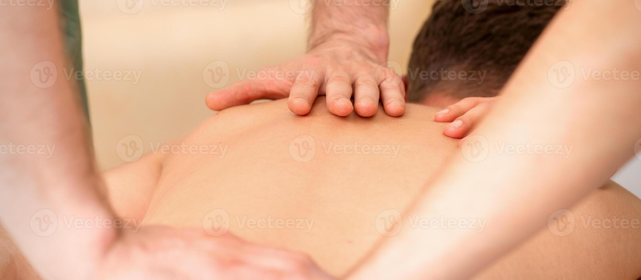 Young man receiving back massage in four hands in spa beauty salon. photo