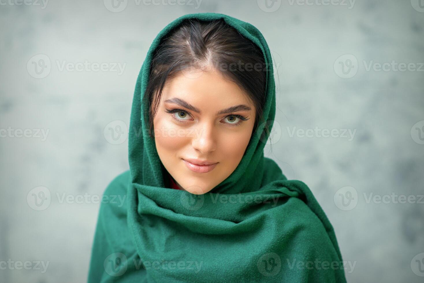 Portrait of a pretty young caucasian woman with makeup in a green headscarf on gray background. photo