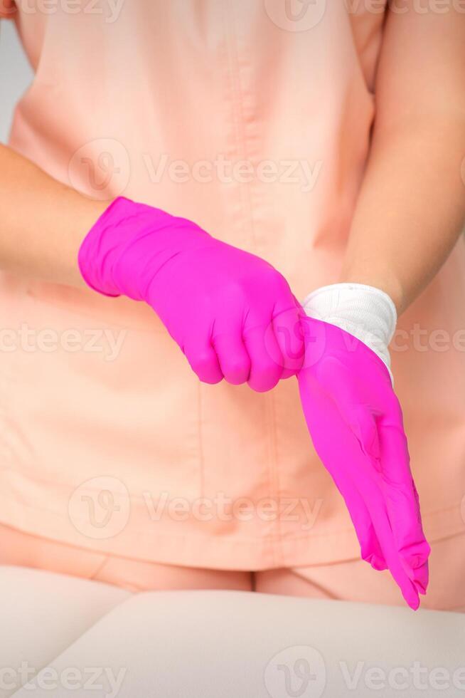 Hand of beautician puts on sterile pink gloves prepares to receive clients indoors. photo