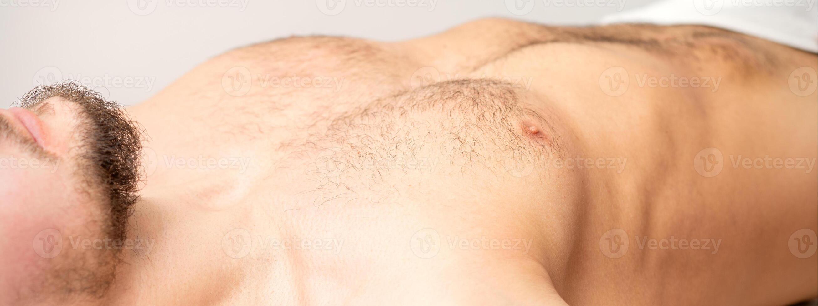 Hairy body, stomach, and chest of a man lying before epilation. photo