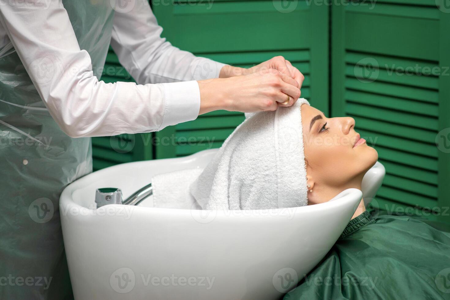 A hairdresser is wrapping a female head in a towel after washing hair in the beauty salon. photo