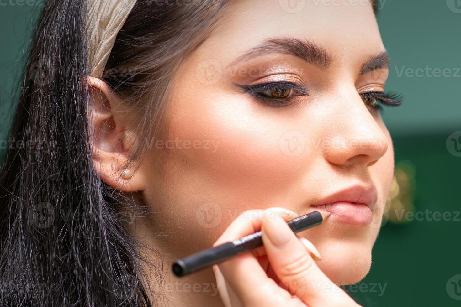 maquillaje profesional artista o cosmetóloga es pintura contorno labios de un joven mujer con un lápiz cerca arriba. foto